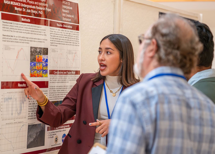 A student stands beside a scientific research poster, gesturing toward a chart as she explains her work to two attendees who are listening closely.