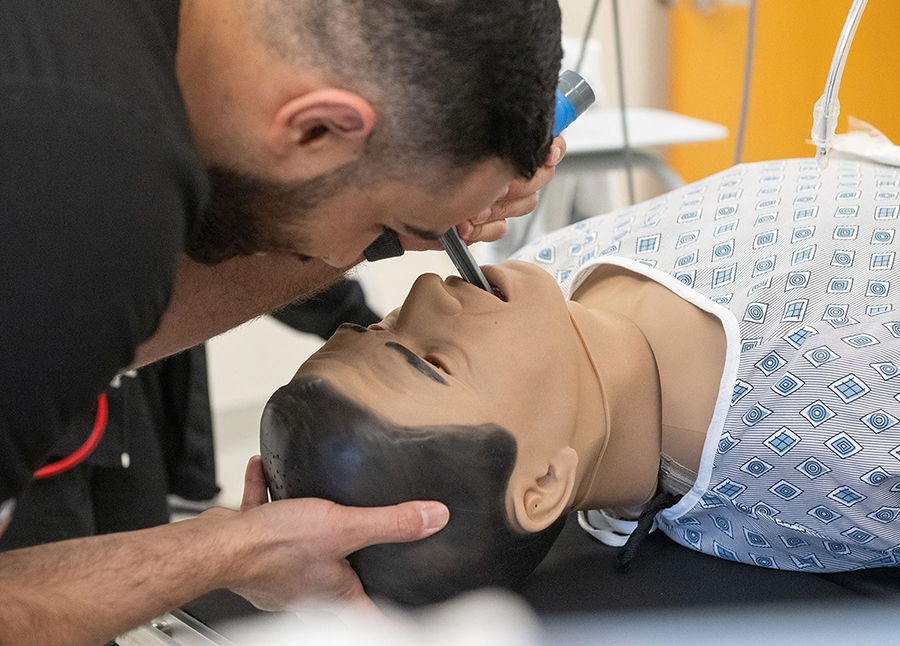 A person practices inserting a breathing tube into a medical training mannequin, holding the mannequin’s head steady while using a laryngoscope during a simulated airway procedure.