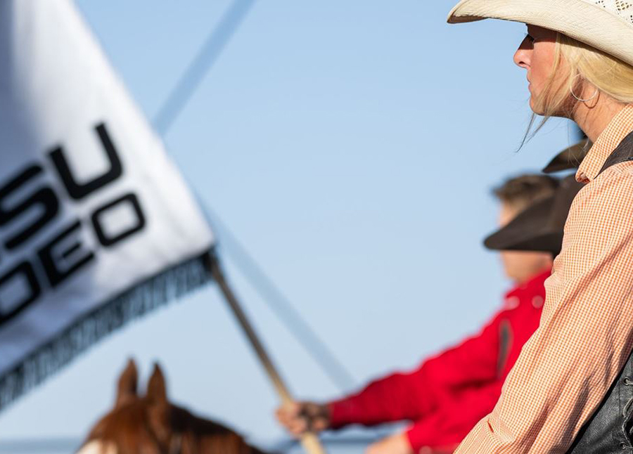 A cowgirl on a horse hold the NMSU rodeo flag.