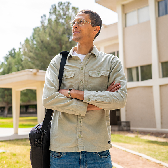 A student stands looking to the side in front of a building on the NMSU main campus