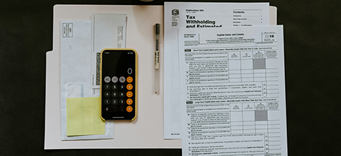 Tax documents and a phone showing the calculator app sitting on a table. 