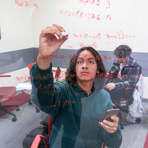 a student working on a math problem on a transparent white board