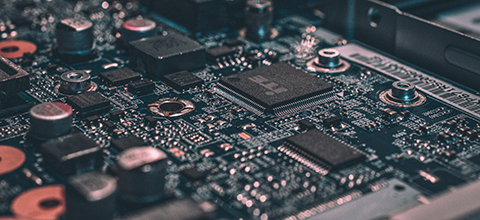 Close-up of a computer circuit board with microchips, capacitors, and intricate electronic pathways in dark tones.