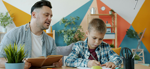 A teacher reading to a male child who is taking notes.