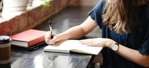 A woman is sitting at a coffee shop writing.